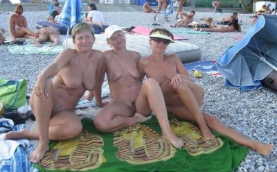 Trzy nagie kobiety rozebrane do rosołu łapią promienie słoneczne na plaży. Dojrzałe panie na plaży nudystów opalają ciałka siedząc na kocyku