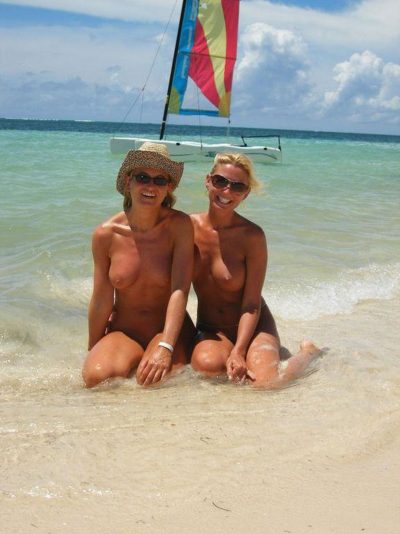 Nagie panie z sexy ciałkami zażywają kąpieli słonecznej podczas wakacji. Dwie kobiety gołe relaksują się na rajskiej plaży