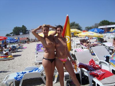 Półnagie dziewczyny na plaży prezentują się mega erotycznie. Dwie fajne laski bez górnej części bikini opalają małe cycki nad morzem